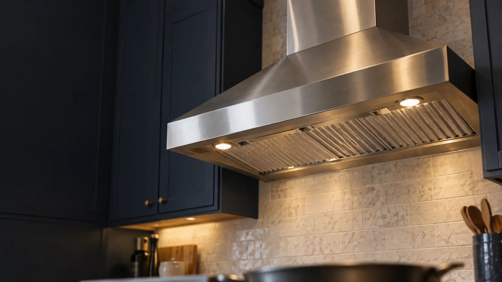A kitchen with a stainless wall-mount range hood and navy painted cabinets, seen from below the range hood.