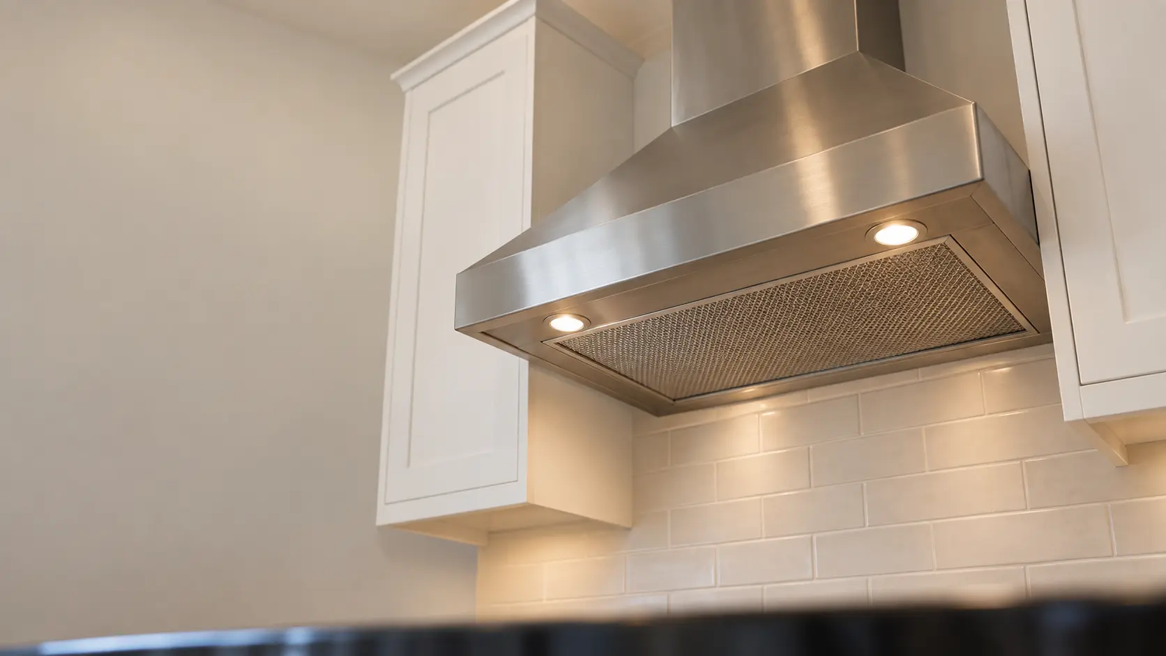 A kitchen with an under-cabinet range hood below wall cabinets and white shaker cabinets, seen from below the range hood.