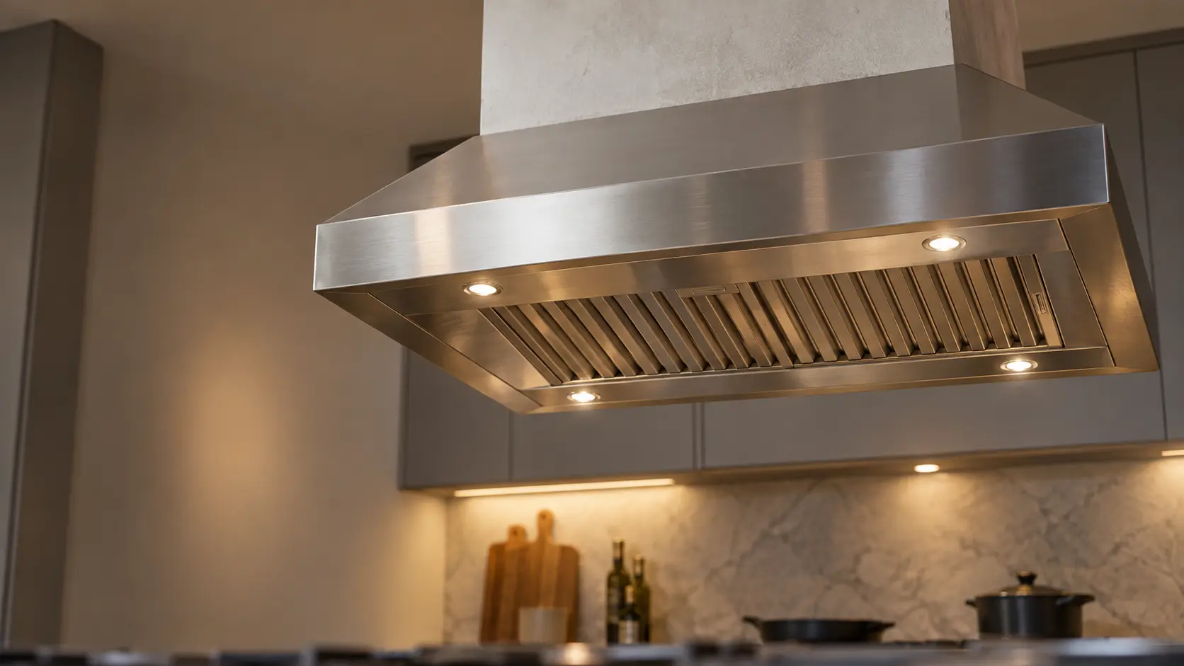 A kitchen island with an island range hood above it and gray slab cabinets, seen from below the range hood.
