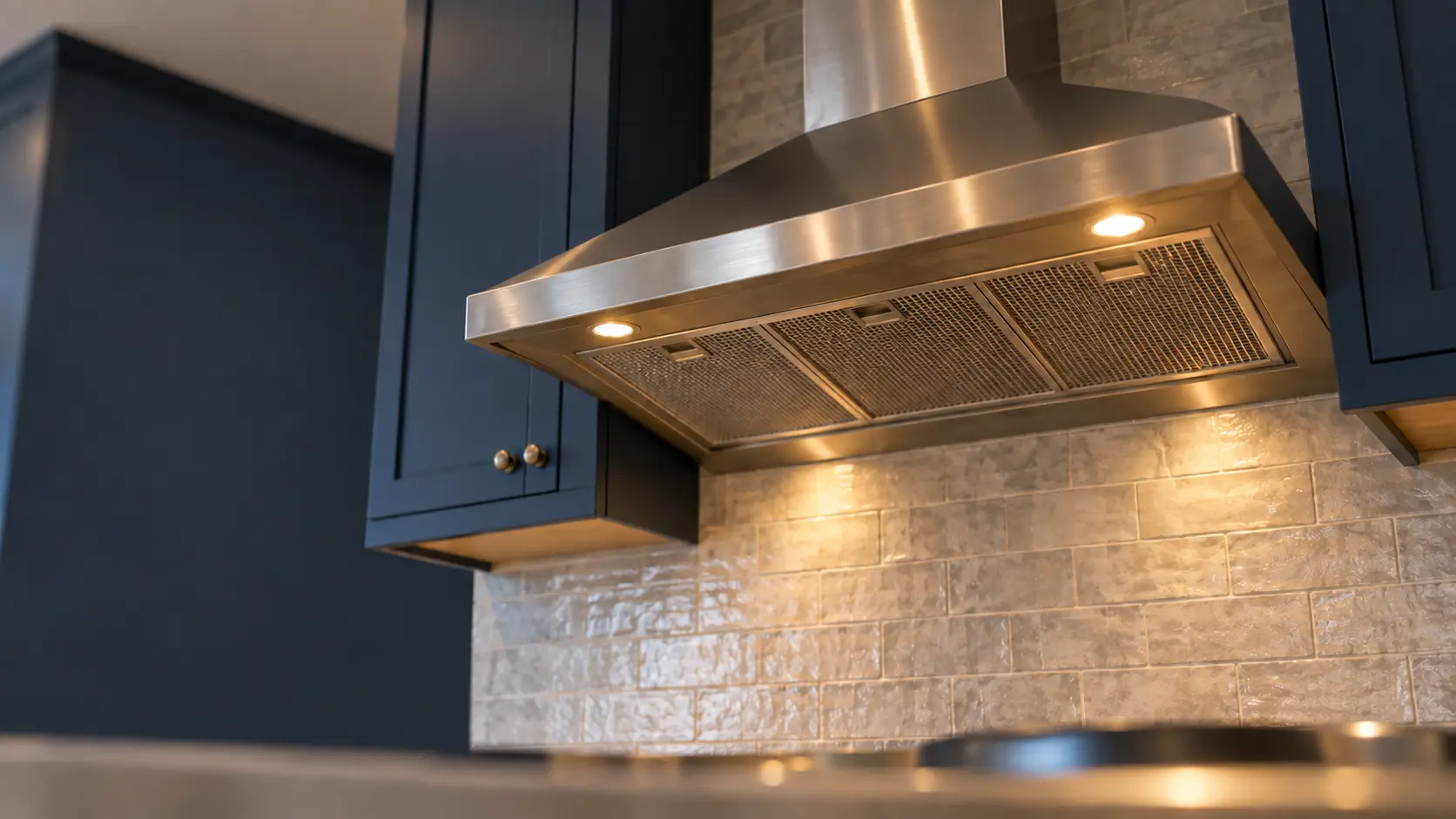 A kitchen with an under-cabinet range hood below wall cabinets and navy painted cabinets, seen from below the range hood.