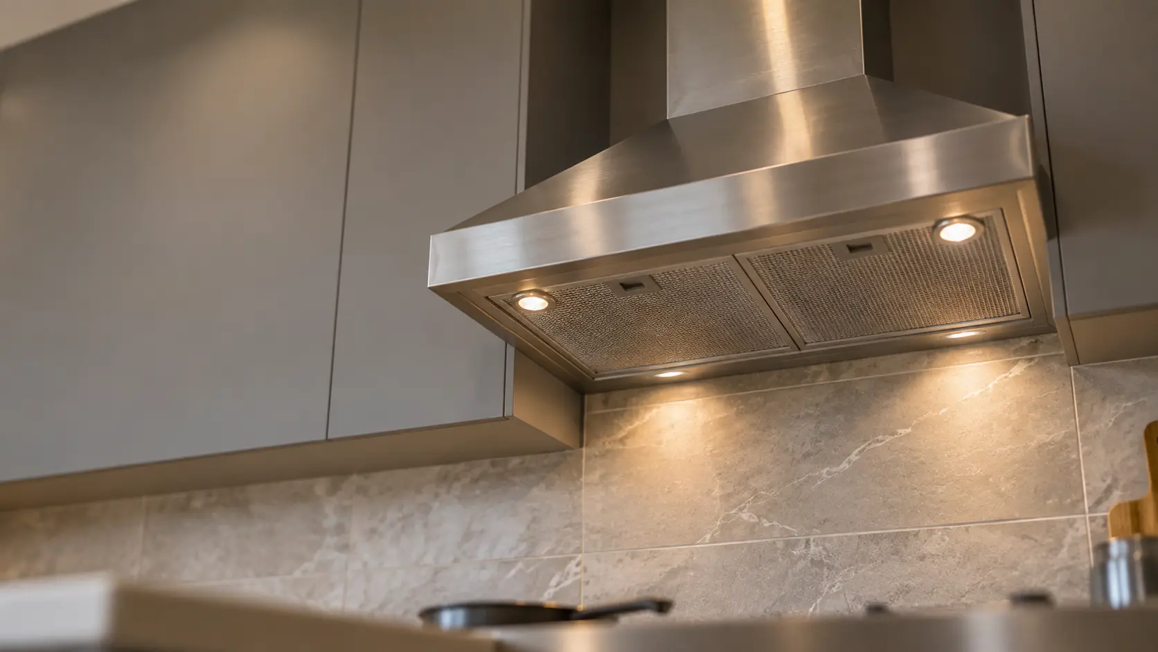 A kitchen with an under-cabinet range hood below wall cabinets and gray slab cabinets, seen from below the range hood.