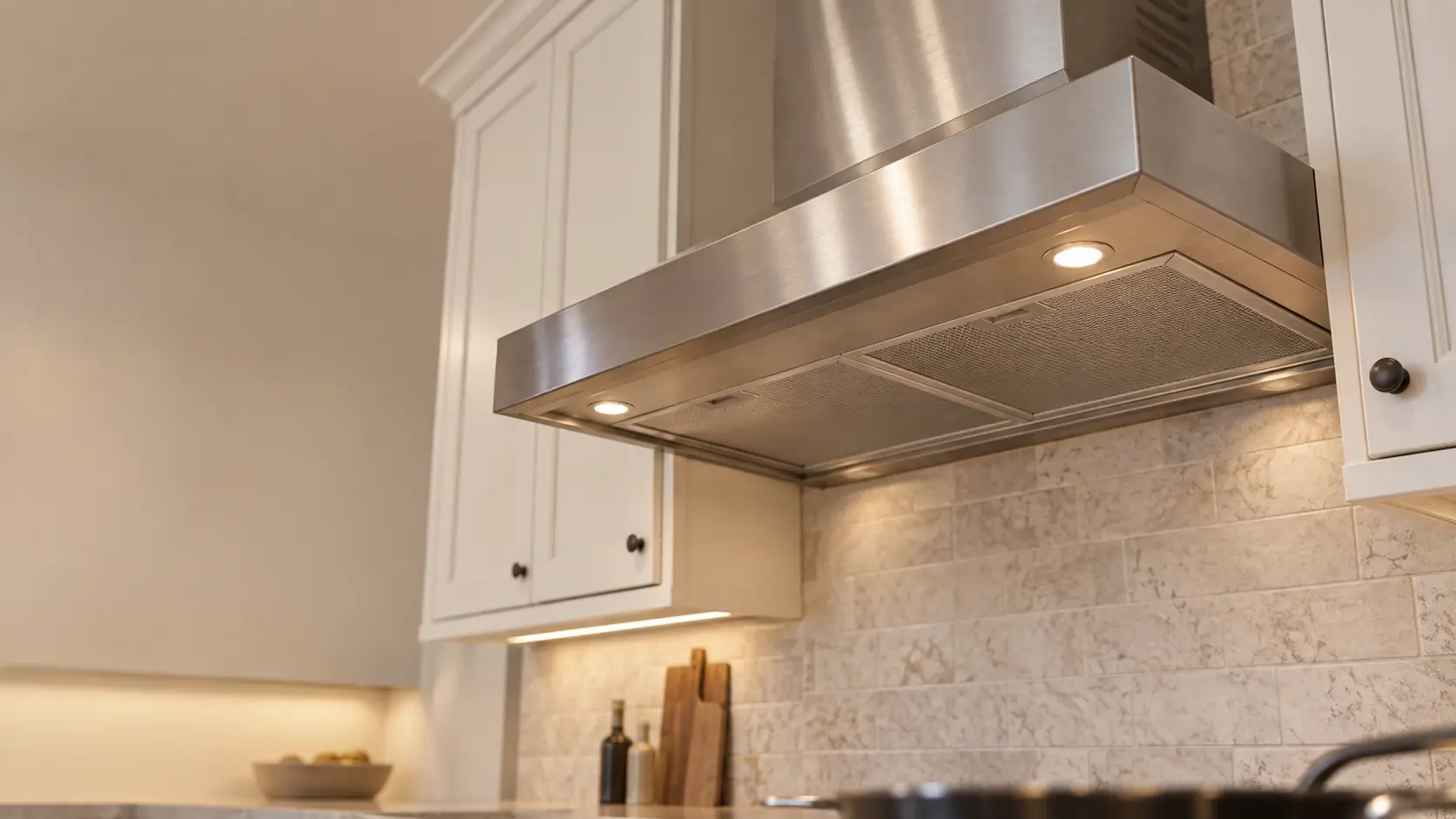 A kitchen with an under-cabinet range hood below wall cabinets and white shaker cabinets, seen from below the range hood.