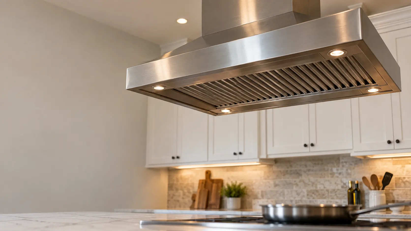A kitchen island with an island range hood above it and white shaker cabinets, seen from below the range hood.