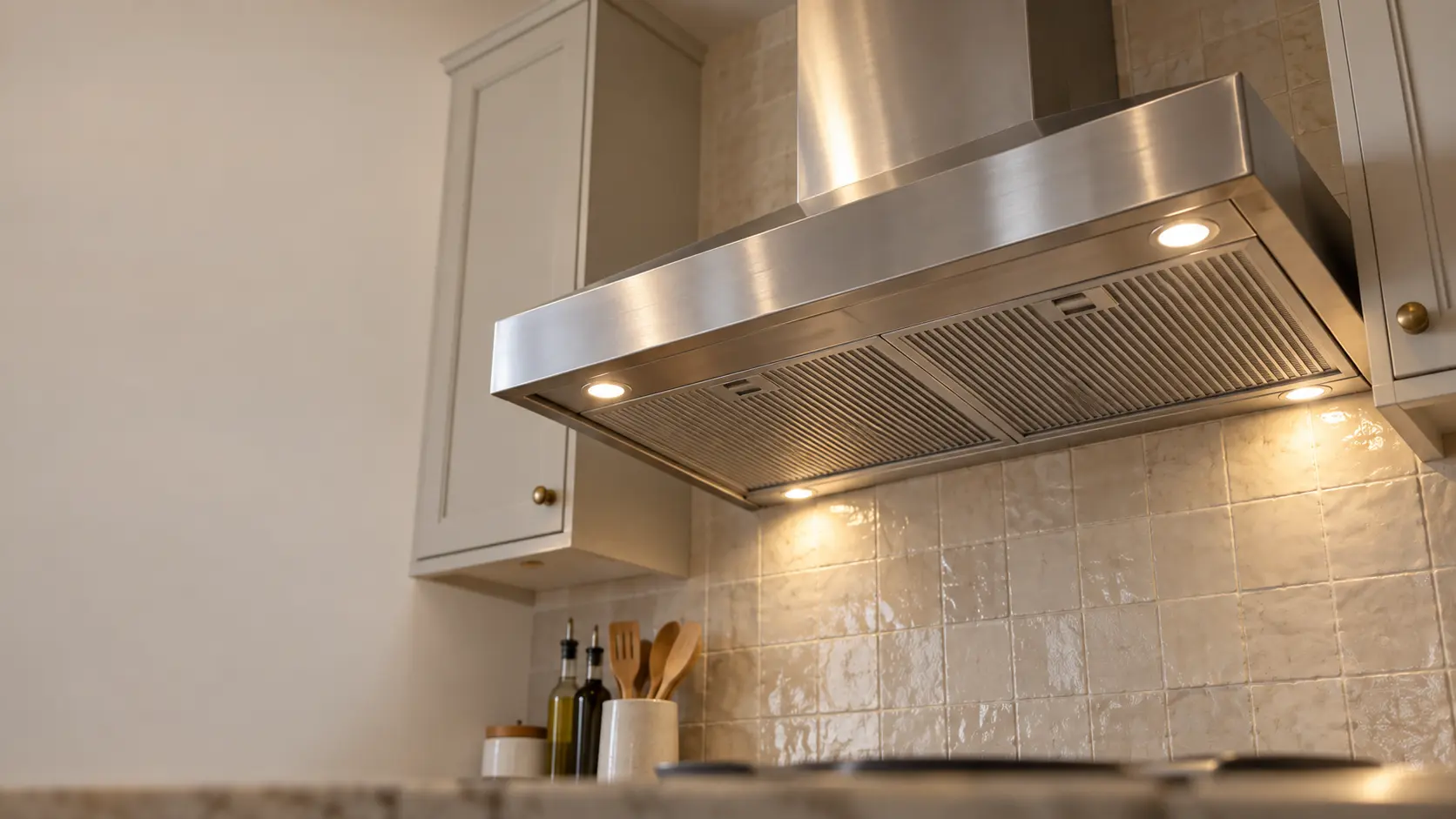 A kitchen with a stainless wall-mount range hood and a zellige tile backsplash, seen from below the range hood.
