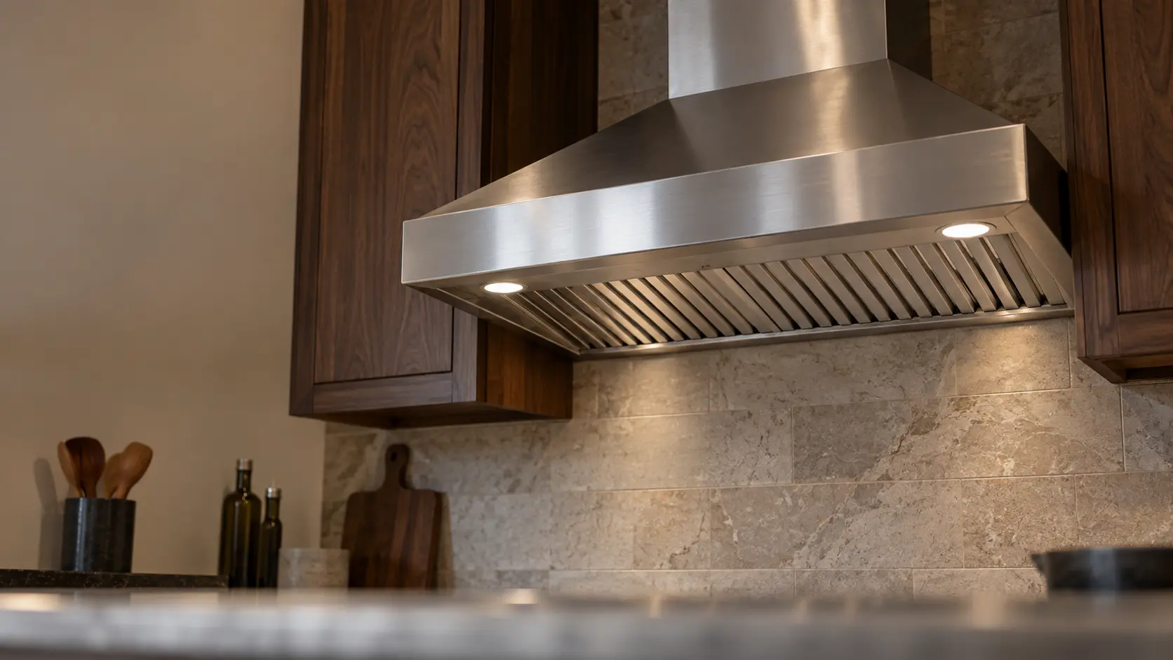 A kitchen with a stainless wall-mount range hood and dark walnut cabinets, seen from below the range hood.