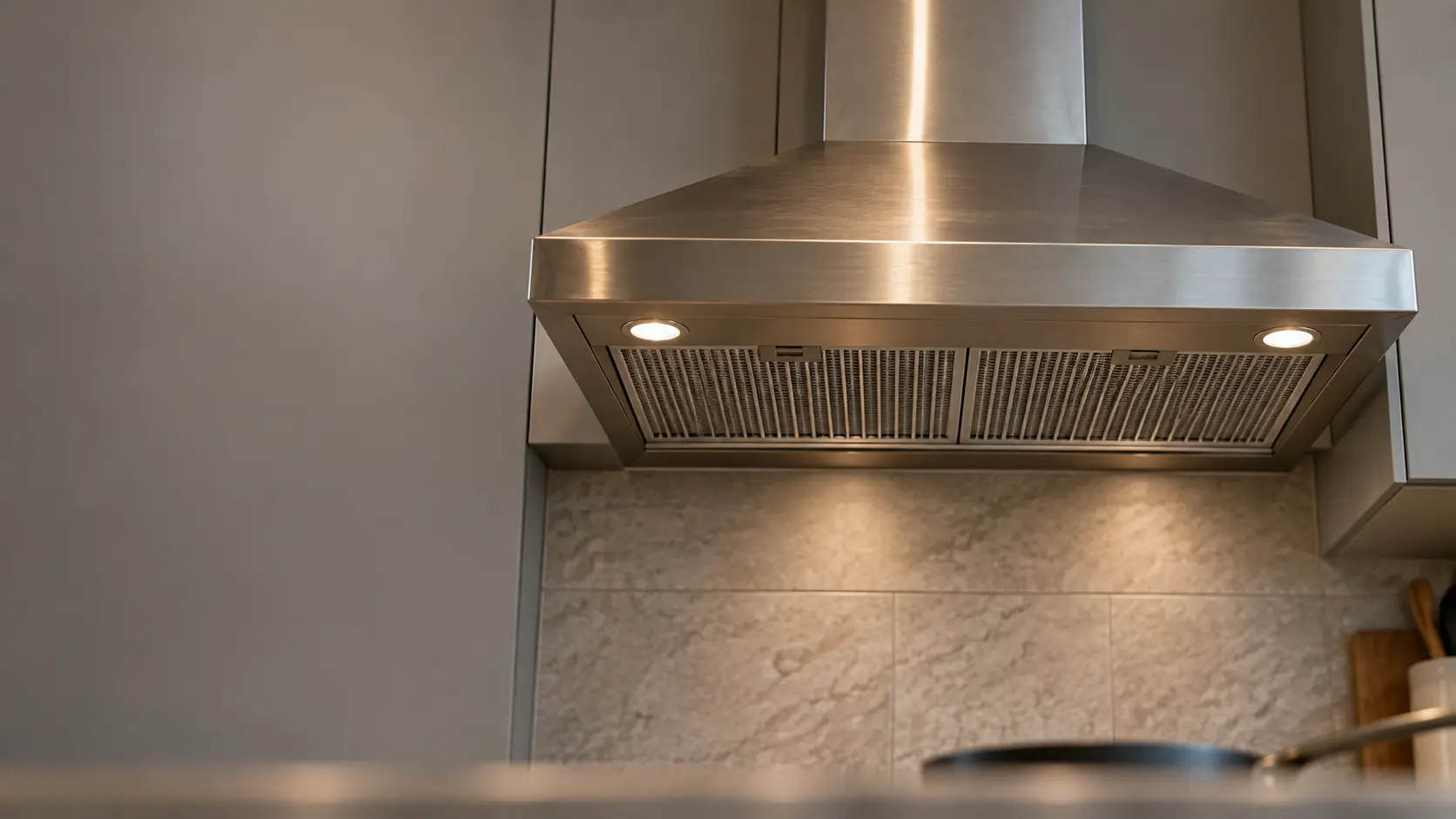 A kitchen with a stainless wall-mount range hood and gray slab cabinets, seen from below the range hood.