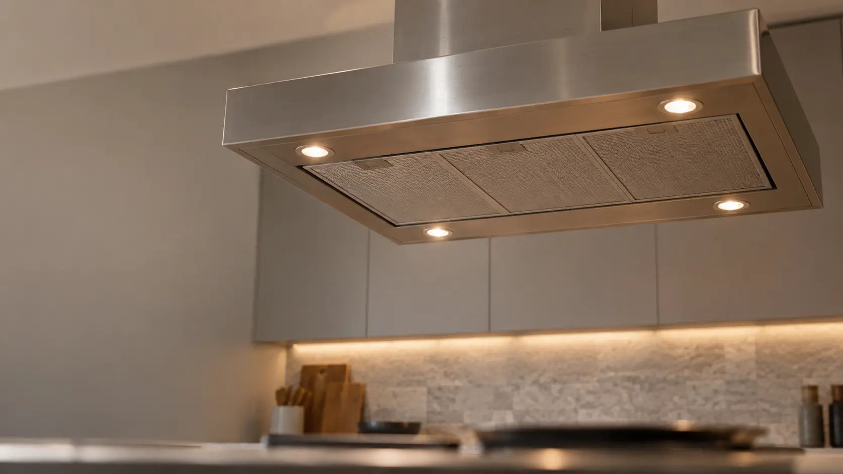 A kitchen island with an island range hood above it and gray slab cabinets, seen from below the range hood.