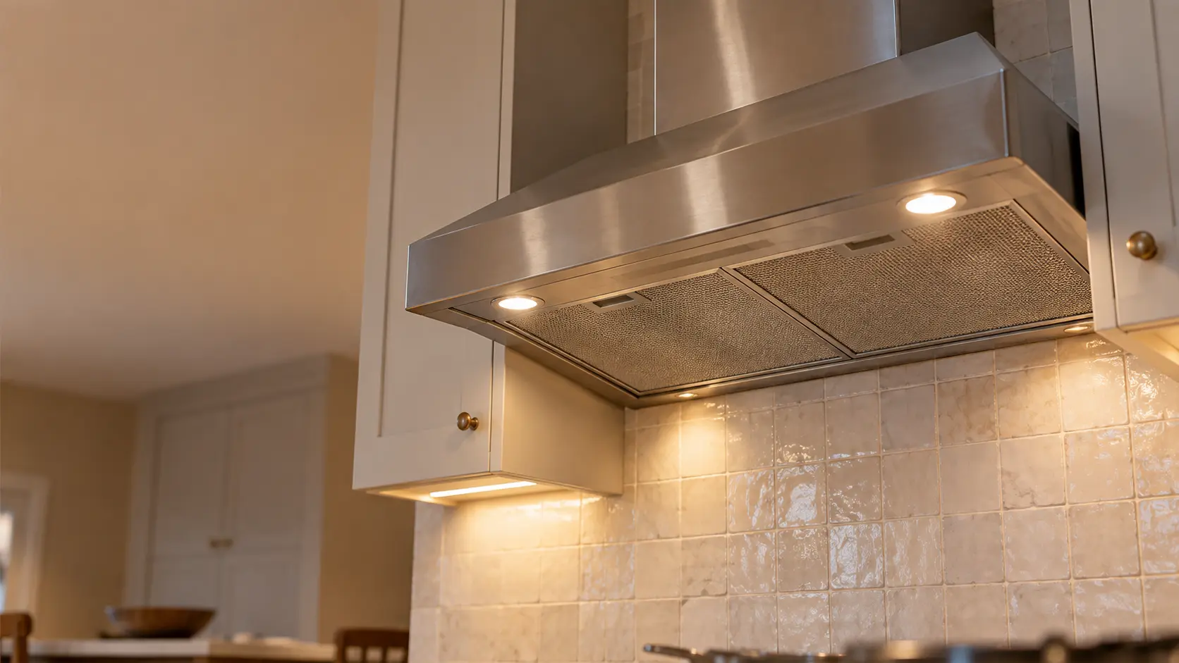 A kitchen with an under-cabinet range hood below wall cabinets and a zellige tile backsplash, seen from below the range hood.
