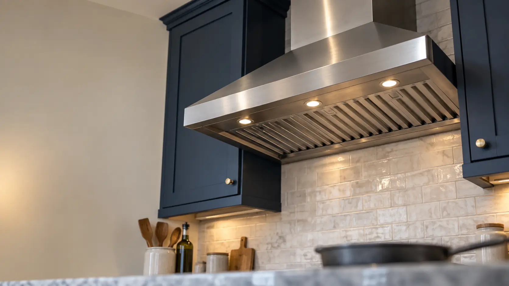 A kitchen with a stainless wall-mount range hood and navy painted cabinets, seen from below the range hood.