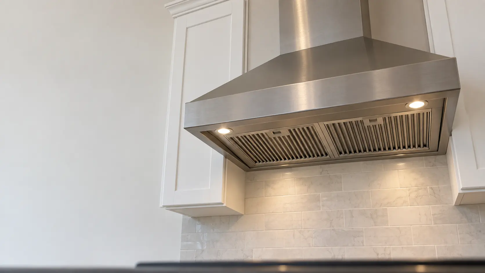 A kitchen with an under-cabinet range hood below wall cabinets and white shaker cabinets, seen from below the range hood.