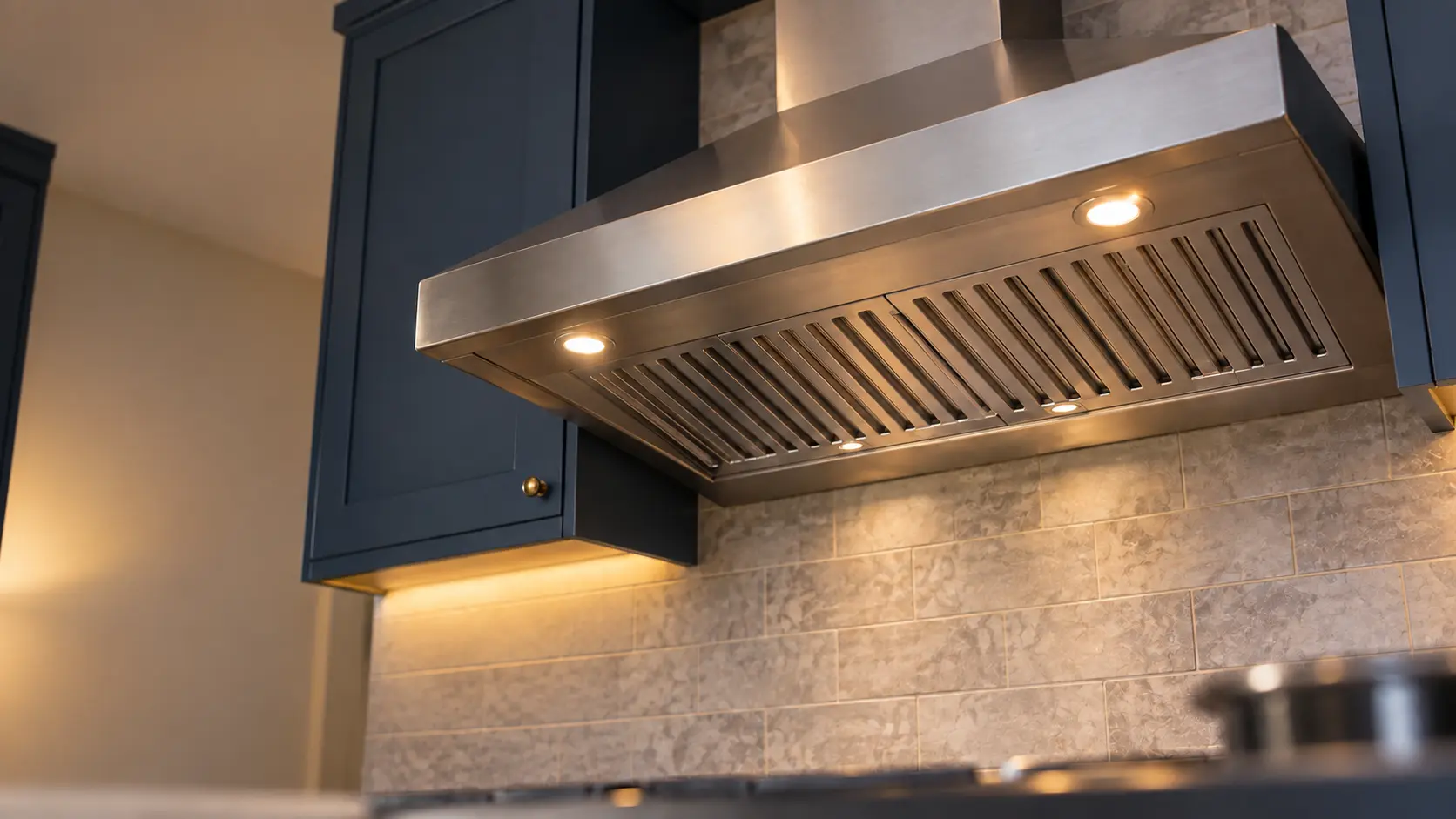 A kitchen with a stainless wall-mount range hood and navy painted cabinets, seen from below the range hood.