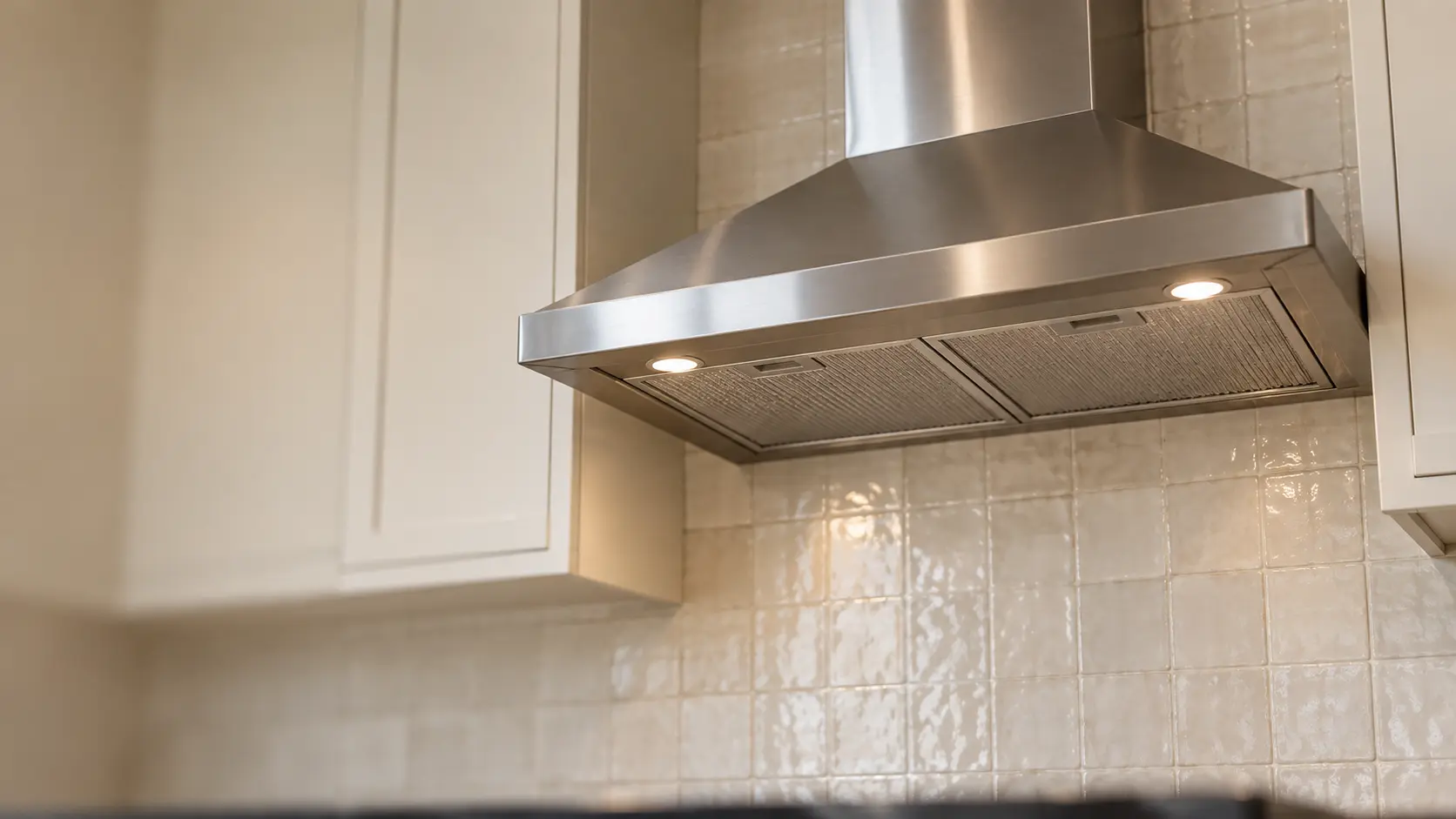 A kitchen with an under-cabinet range hood below wall cabinets and a zellige tile backsplash, seen from below the range hood.