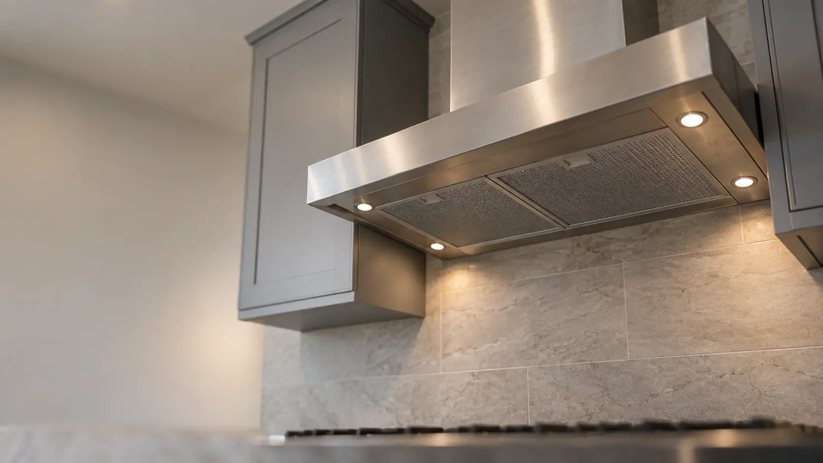 A kitchen with an under-cabinet range hood below wall cabinets and gray slab cabinets, seen from below the range hood.