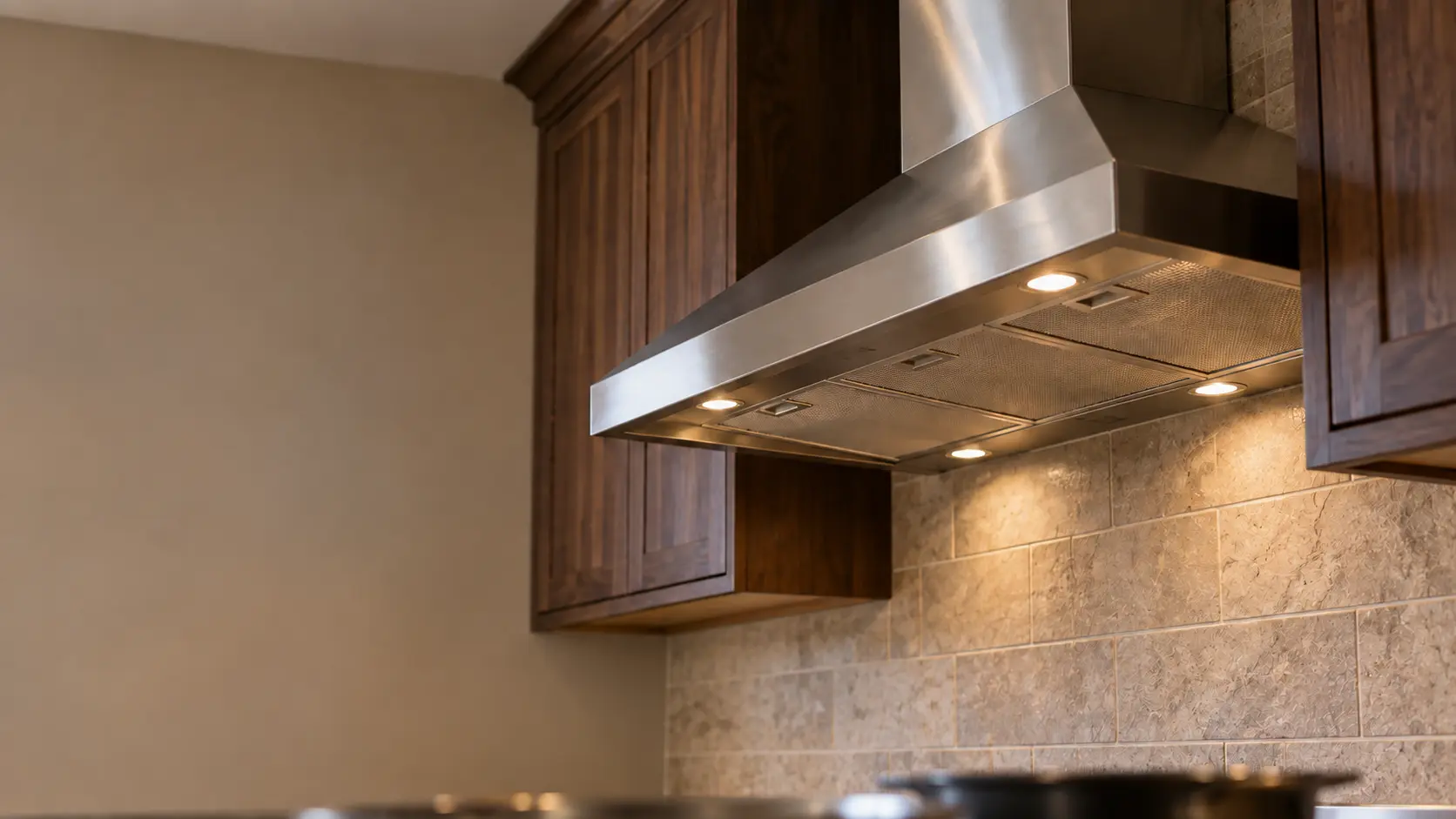 A kitchen with a stainless wall-mount range hood and dark walnut cabinets, seen from below the range hood.