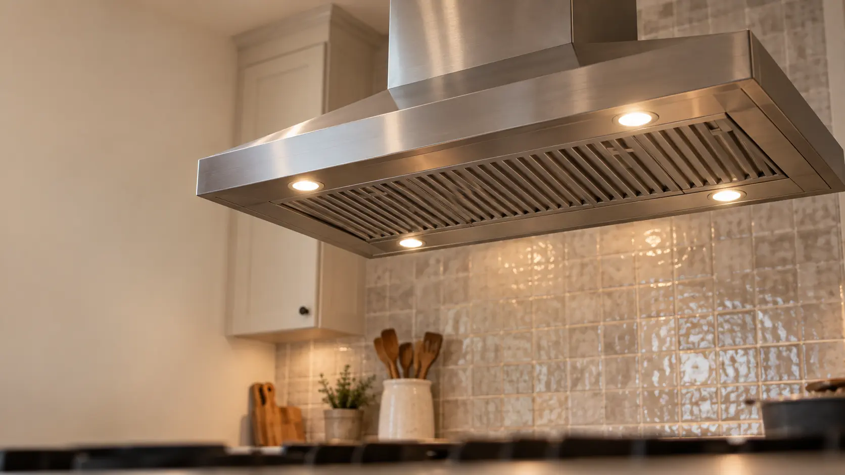 A kitchen island with an island range hood above it and a zellige tile backsplash, seen from below the range hood.
