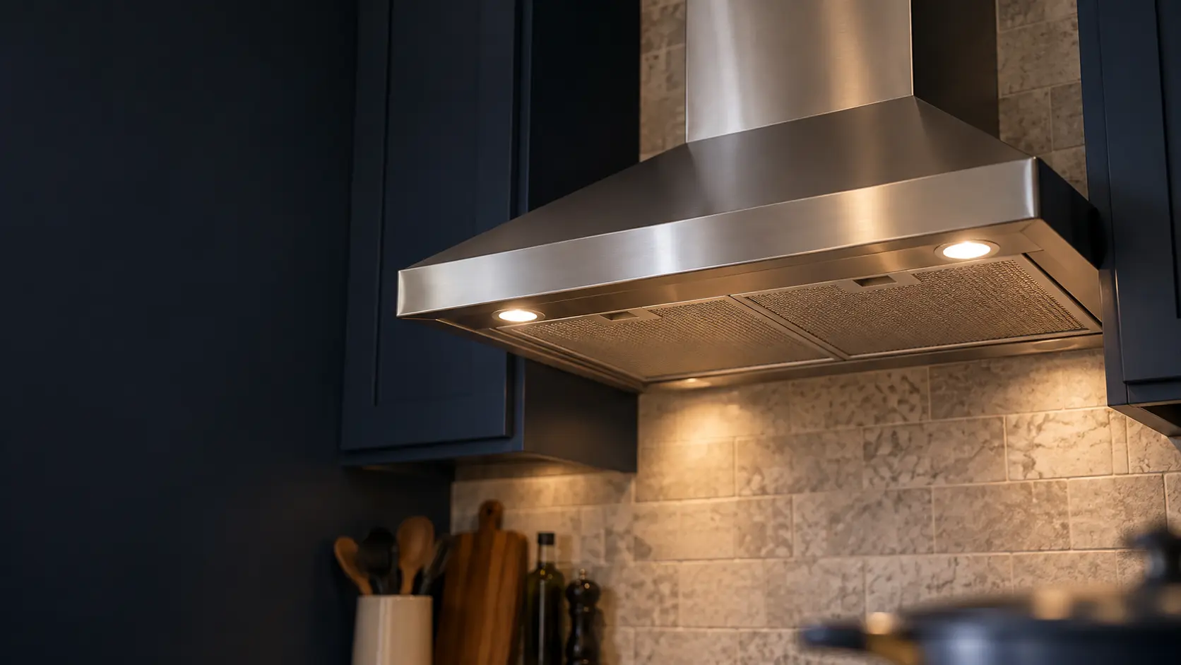 A kitchen with an under-cabinet range hood below wall cabinets and navy painted cabinets, seen from below the range hood.