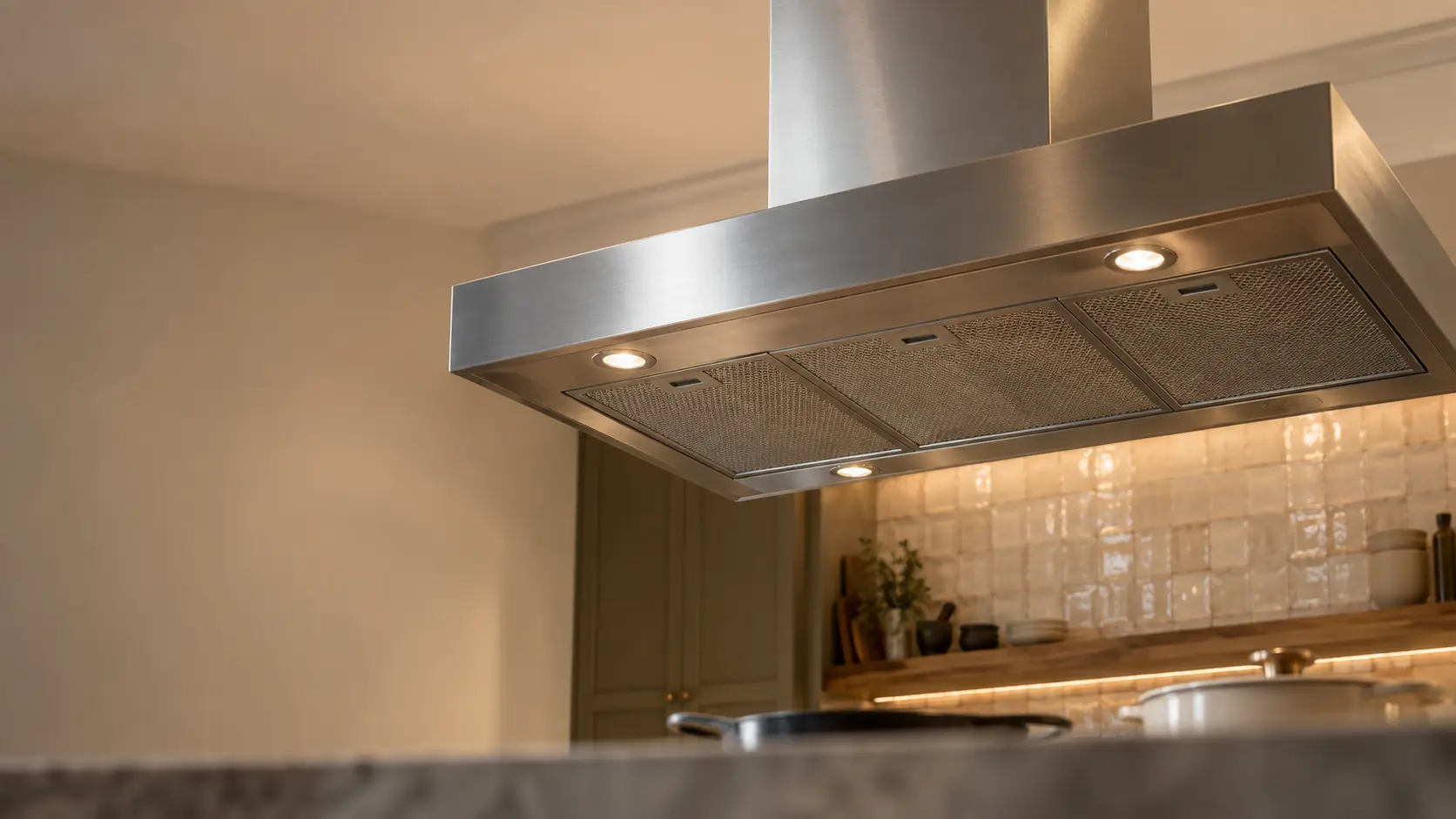 A kitchen island with an island range hood above it and a zellige tile backsplash, seen from below the range hood.