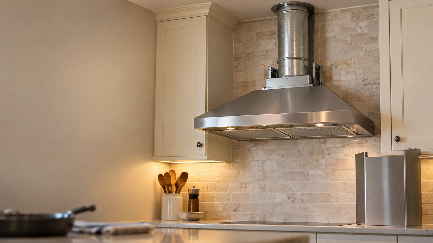 A round metal duct rising from the top of a range hood into the ceiling, the chimney cover set aside.