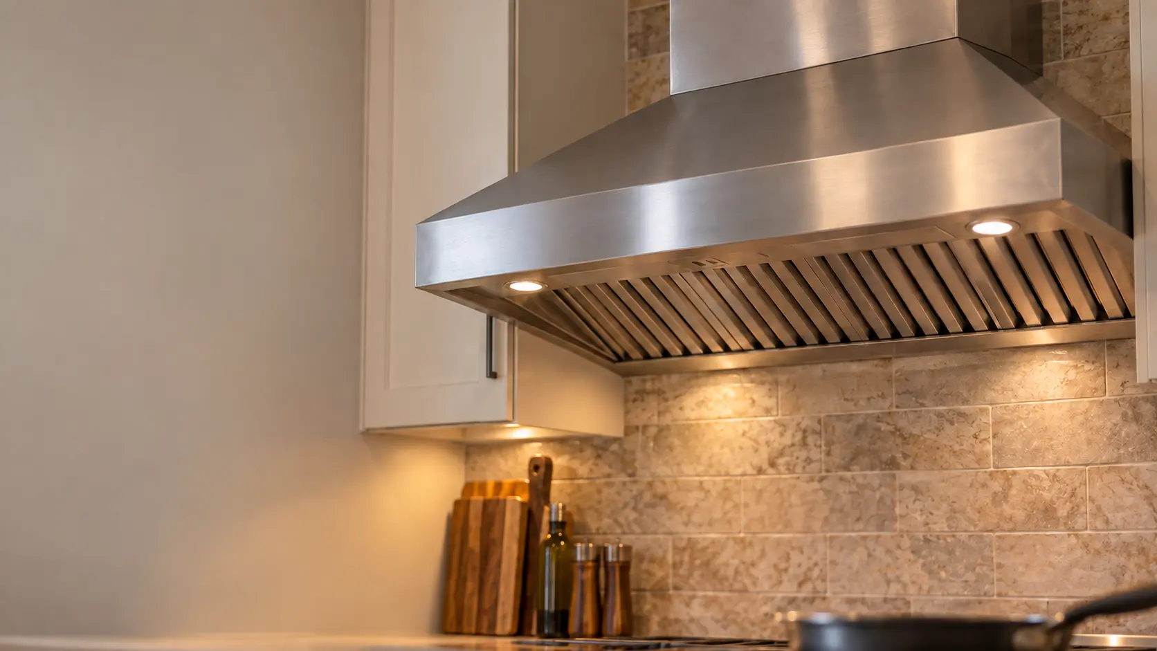 The brushed stainless canopy and baffle filters of a range hood filling the frame, soft light.