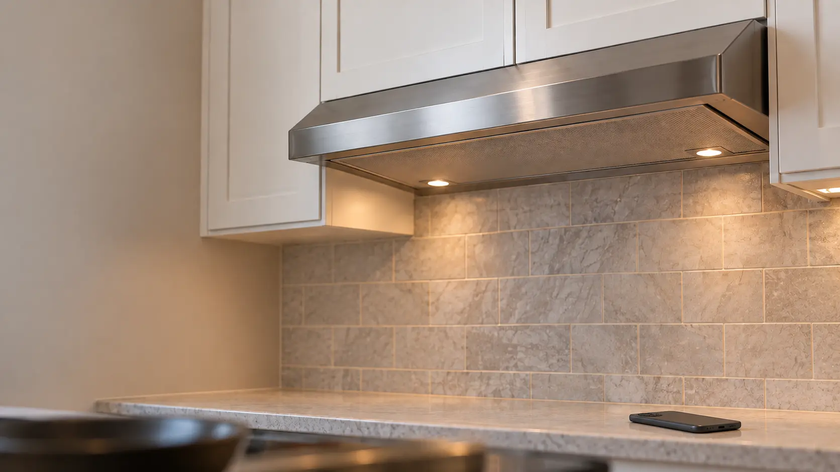 A kitchen counter with a phone lying face down on it below an under-cabinet range hood.