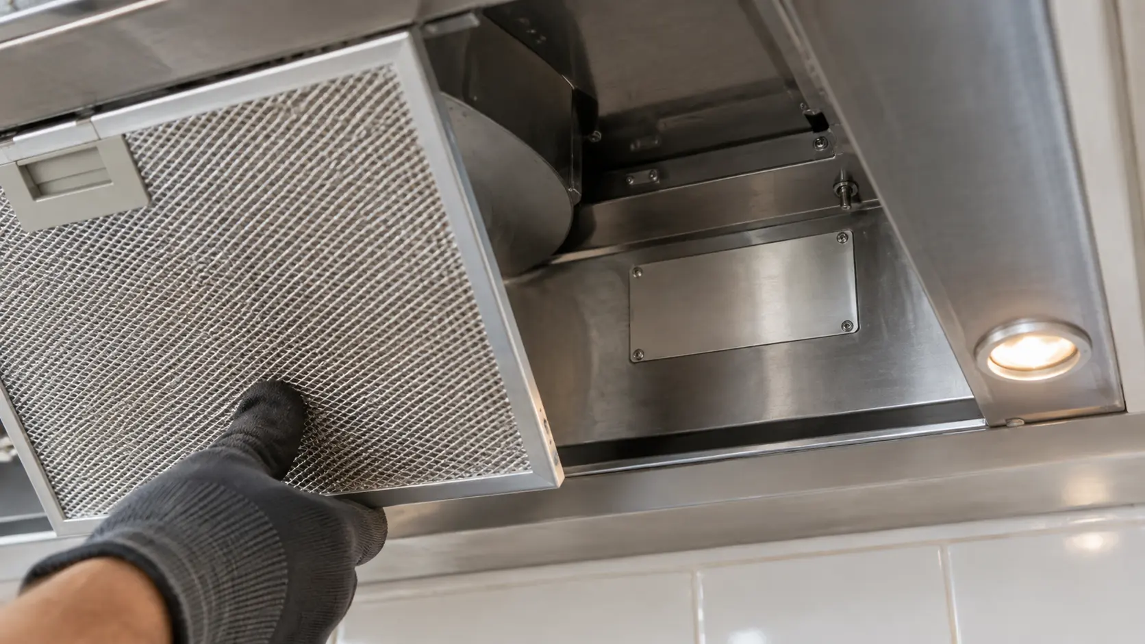 Close on a small blank metal plate with no characters inside a range hood canopy, its filter lifted out.