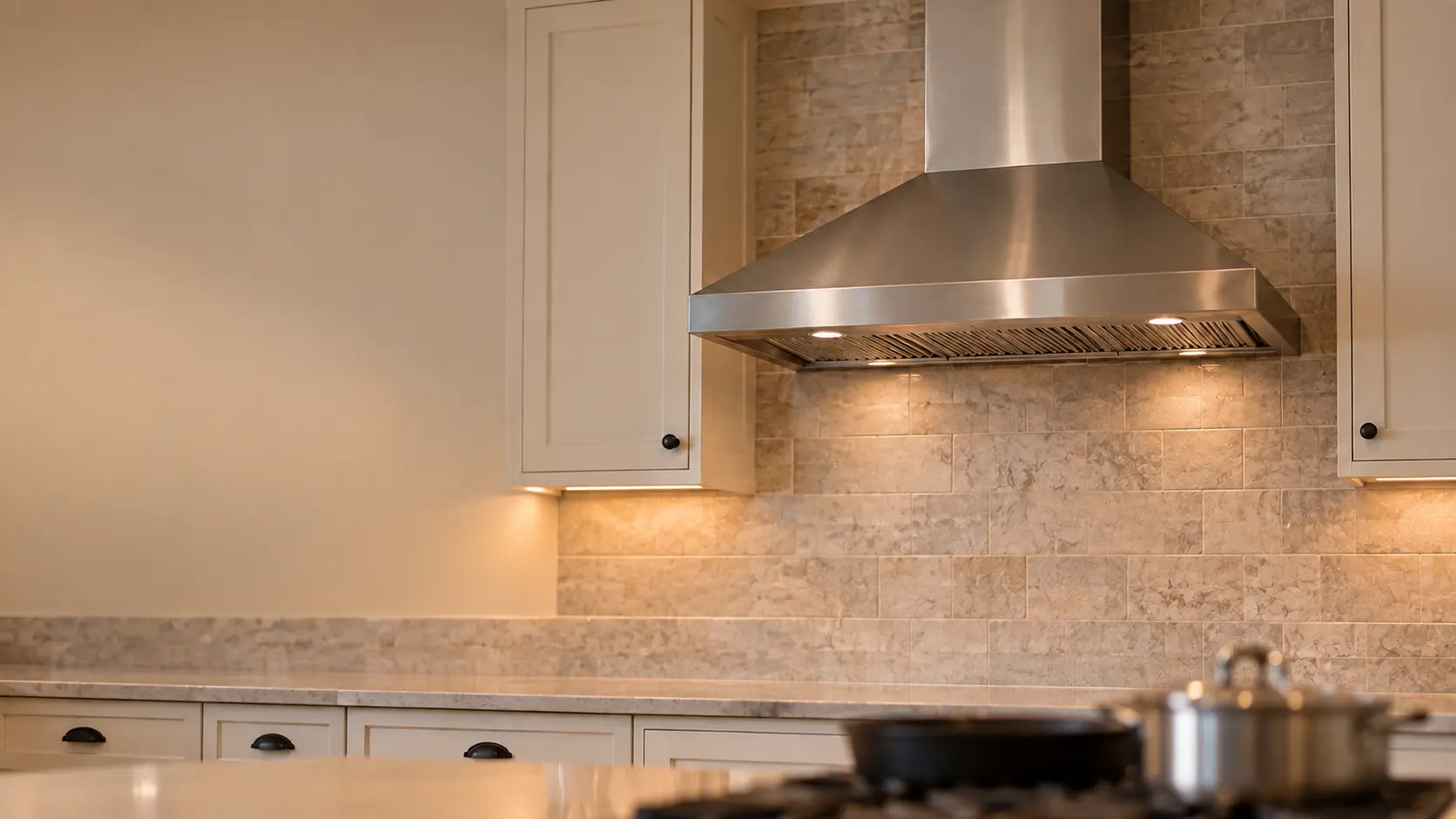 A family home's kitchen with a wall-mount range hood above the cooking area, seen from across the room.