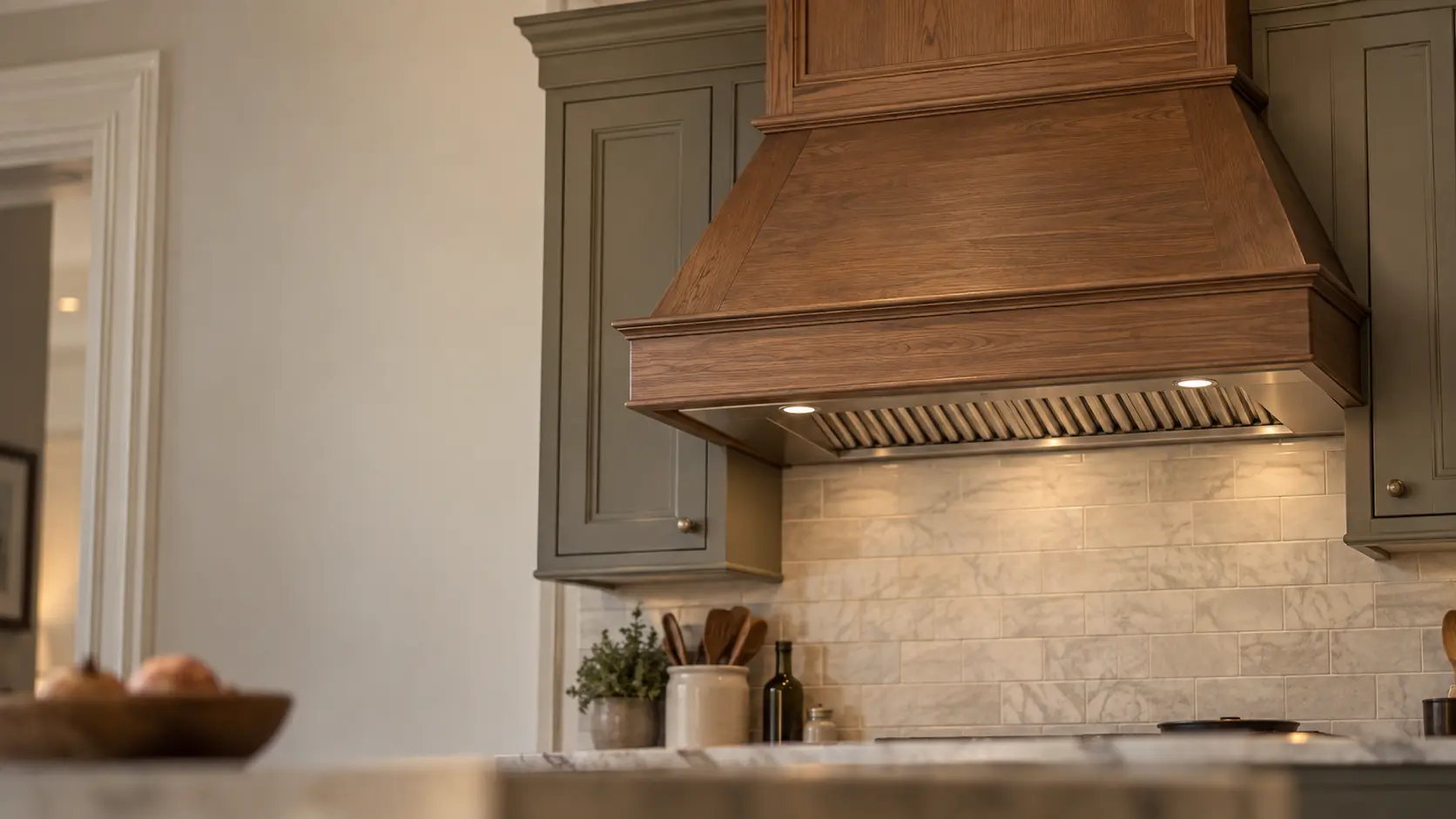 A Bay Area Victorian's remodeled kitchen with a wood-clad range hood with a stainless insert, seen from across the room.